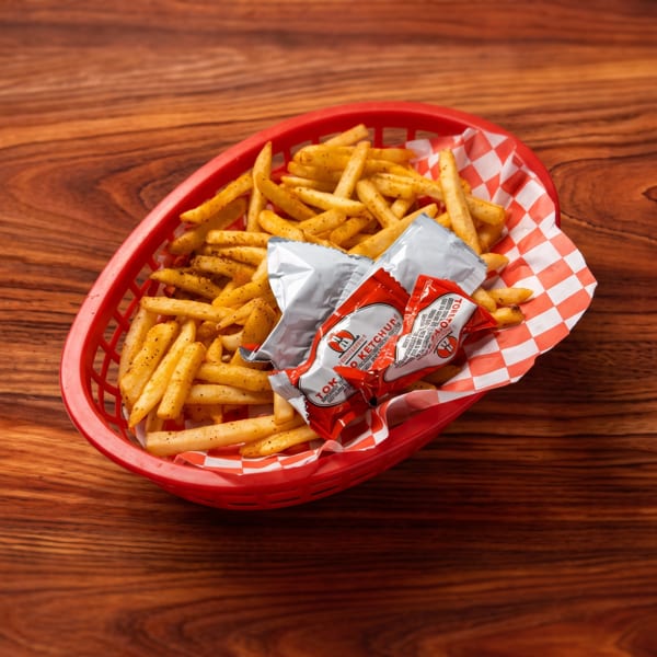 A red basket of seasoned french fries and ketchup packets on a dark wooden table.