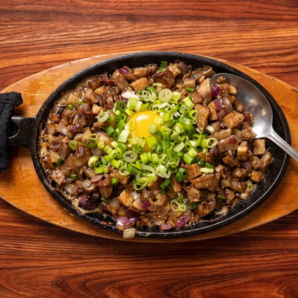 Sizzling sisig with a raw egg yolk and green onions, served on a wooden board with a spoon.