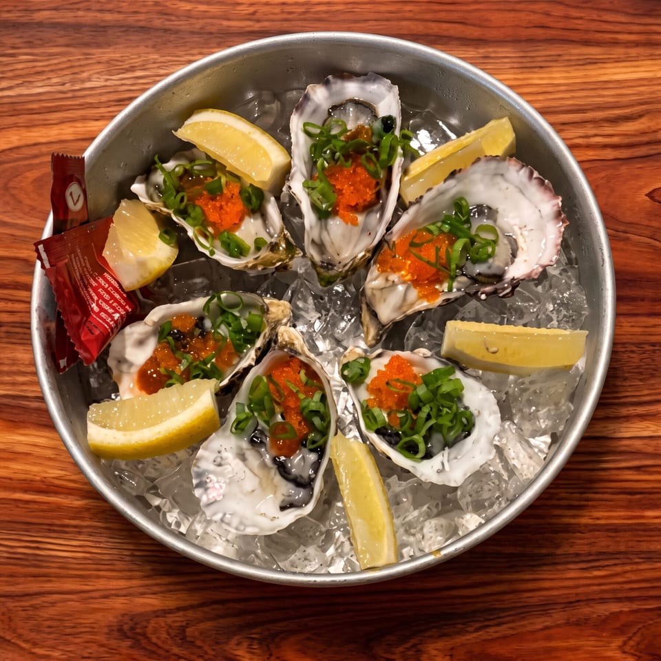 Six fresh oysters on ice with roe, green onions, and lemon in a metal platter.